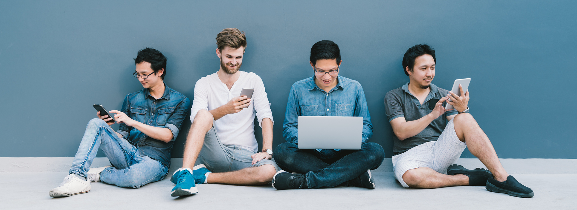 un groupe de jeunes hommes assis par terre à l'aide d'appareils mobiles