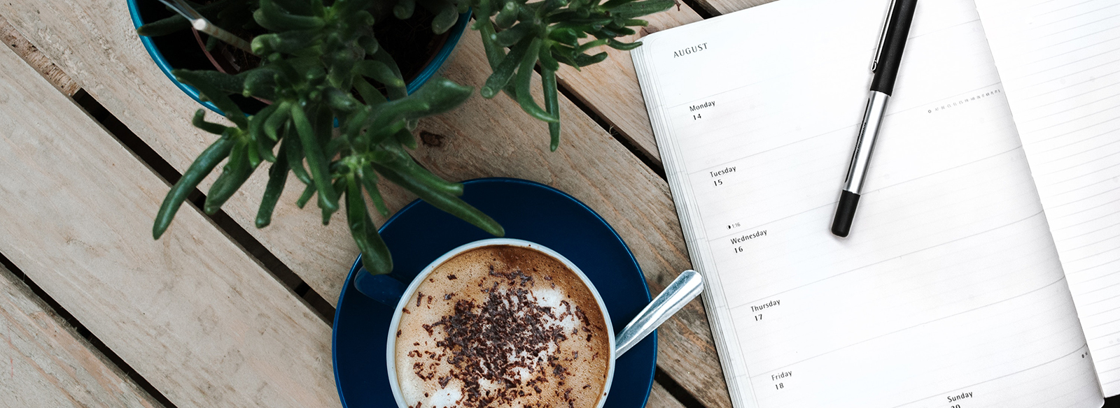 a planner, a pen, a coffee and a pant on top of a table