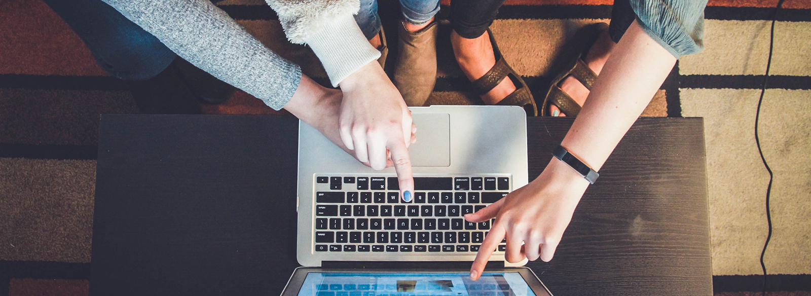 Laptop surrounded by three individuals pointing towards it.