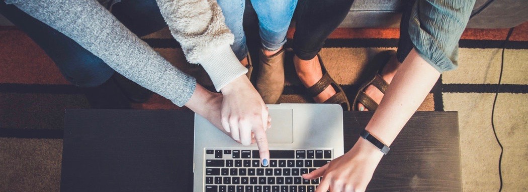 Laptop surrounded by three individuals pointing towards it.