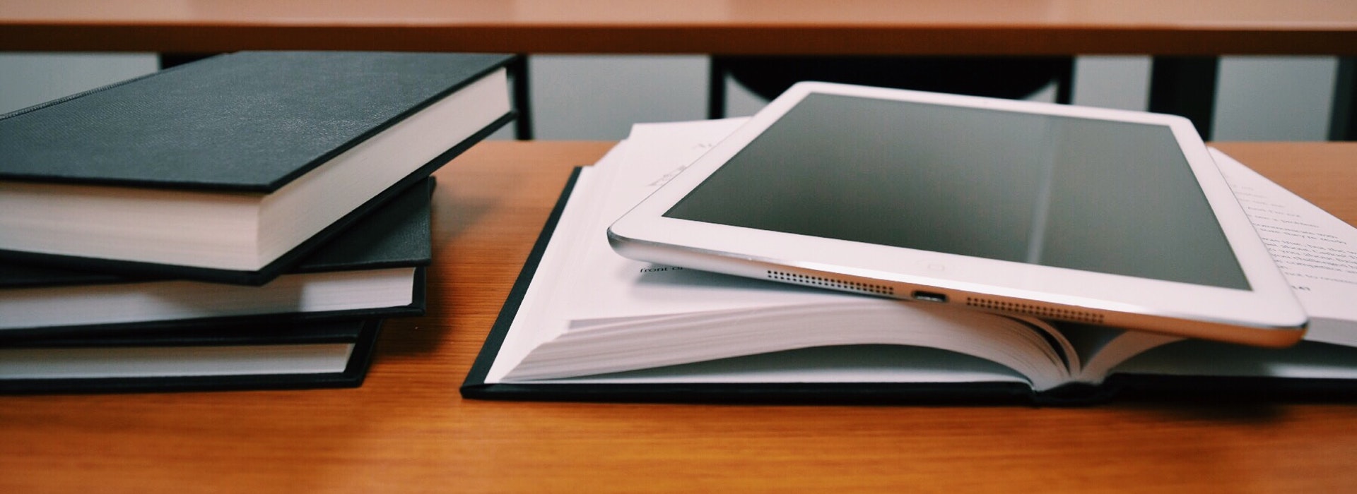 Black books and a white iPad stacked on a wooden desk.