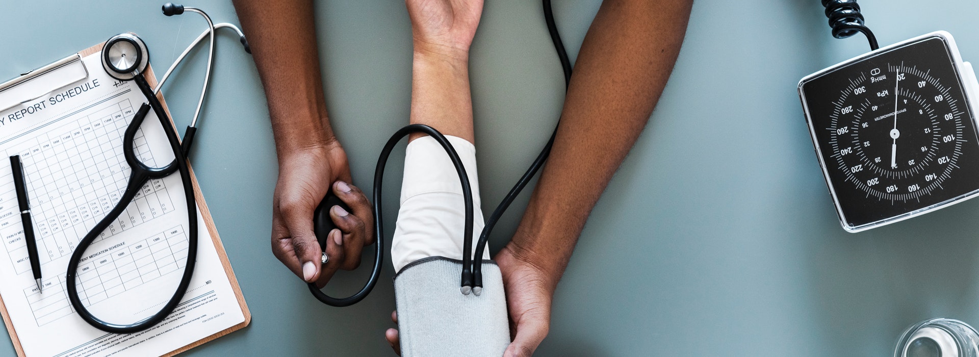 English description: Bird’s eye view of a nurse’s hands using a black blood pressure monitor on a patient’s arm. description en français: vue des mains d’une infirmière qui utilise un tensiomètre noir sur le bras d’un patient.