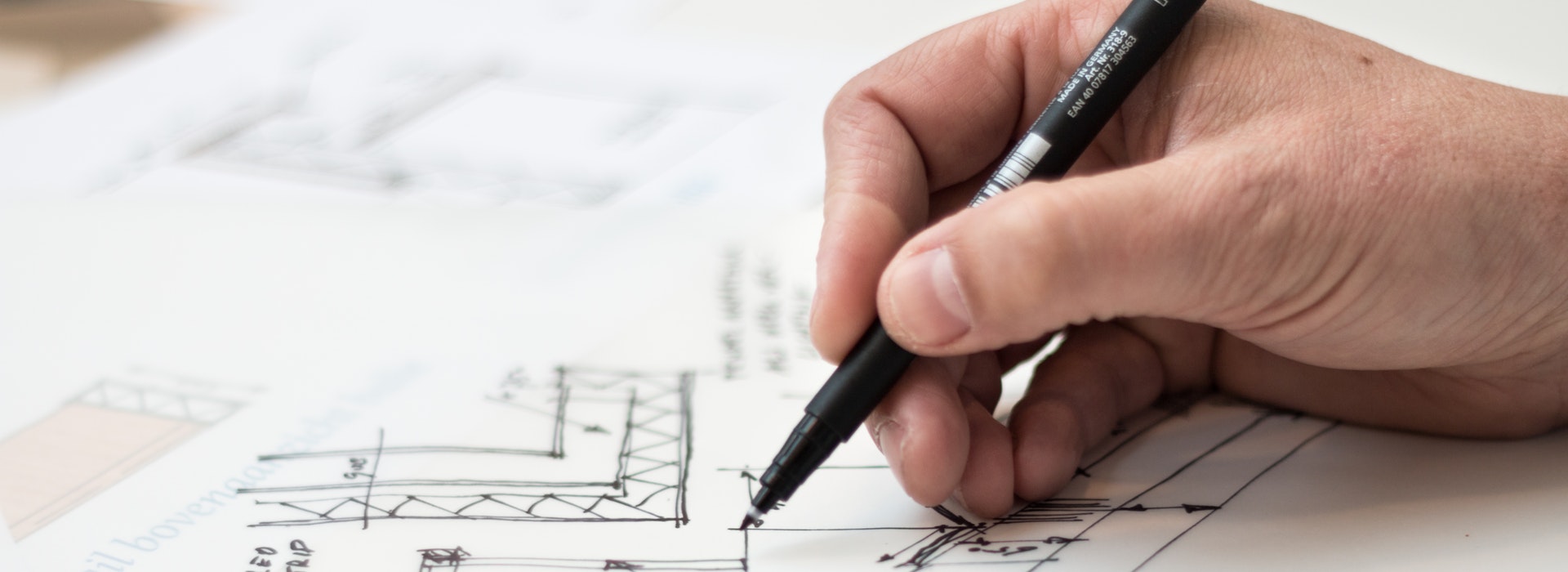 A man’s hand holds a black pen over an architectural diagram