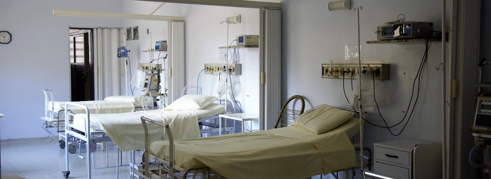 Three empty hospital beds sit beside each other in a hospital room