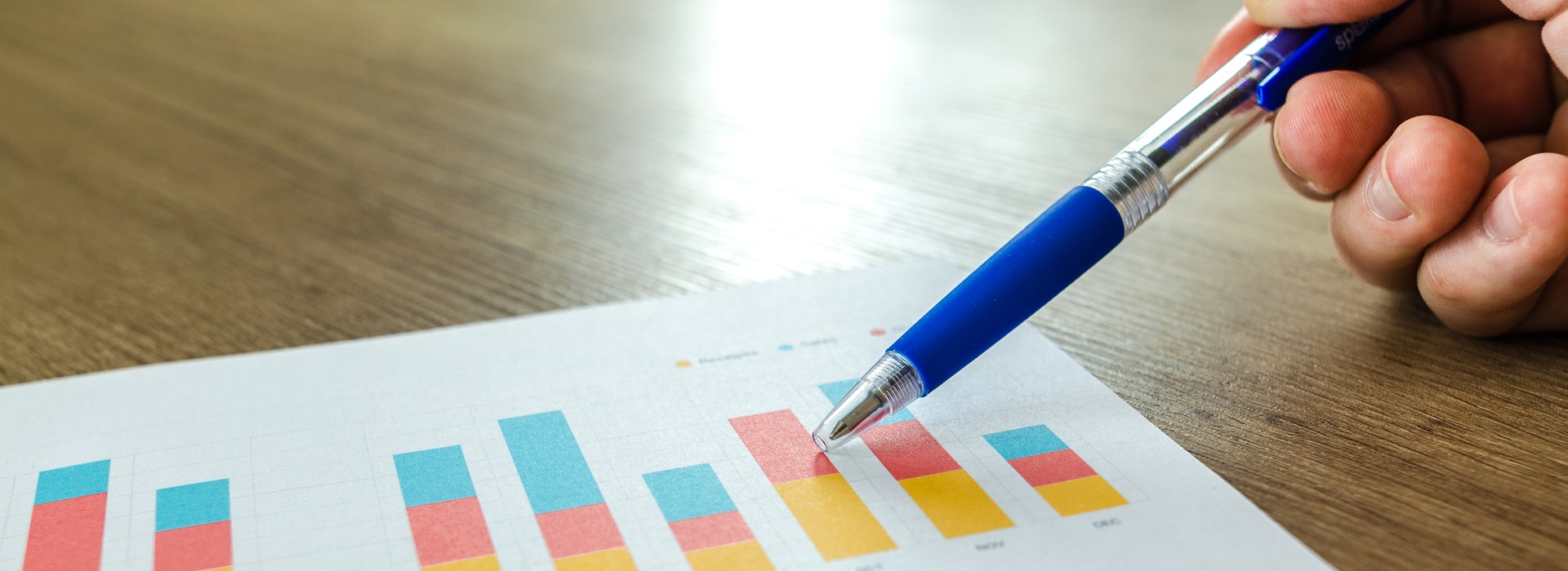 A hand holds a pen over a chart showing a blue and orange bar graph