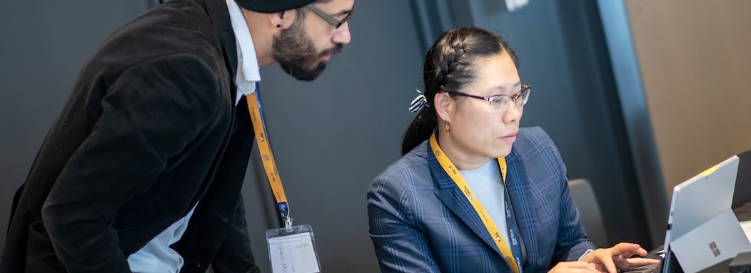 Photo of a woman typing in a business suit types on a laptop, while a man reads over her shoulder