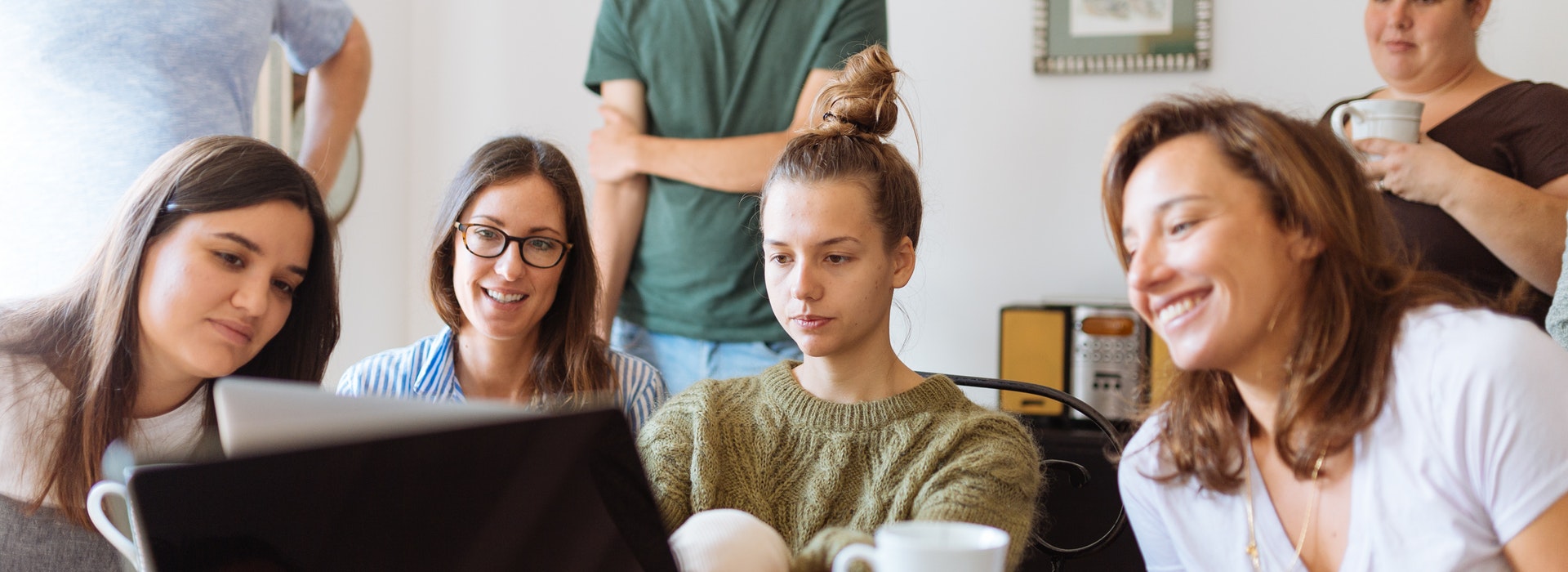 A group of college students peer at a laptop, smiling