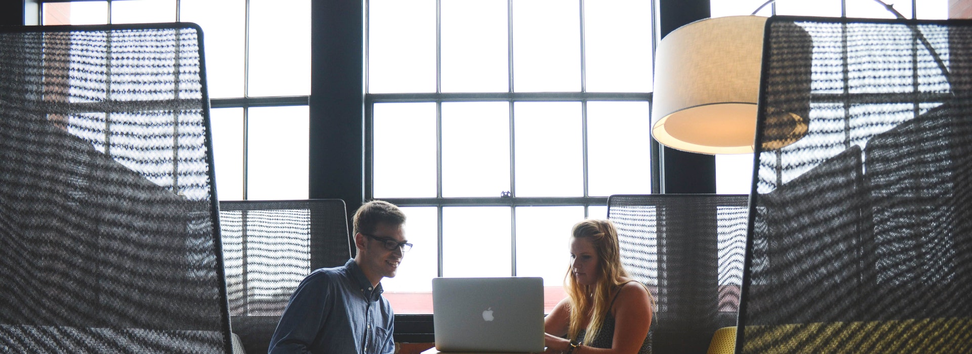 Two young professionals sit at a booth sharing a laptop