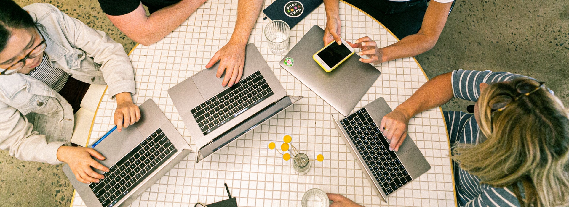 Photo of students’ hands typing on laptops around a table