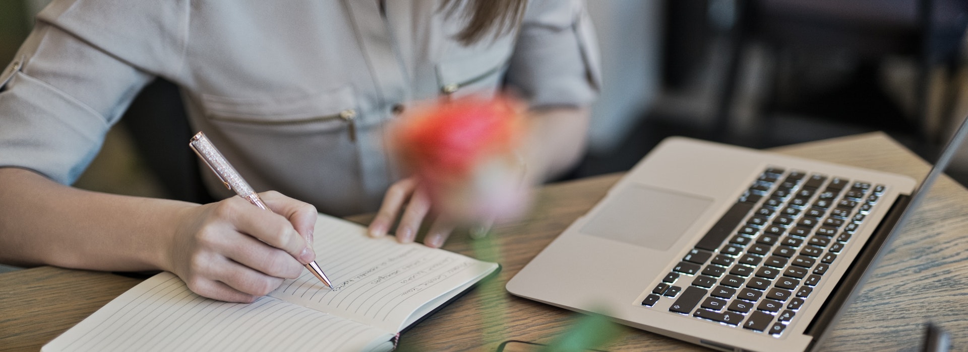 Closeup photo of a woman's hands, writing in a notebook beside with a laptop