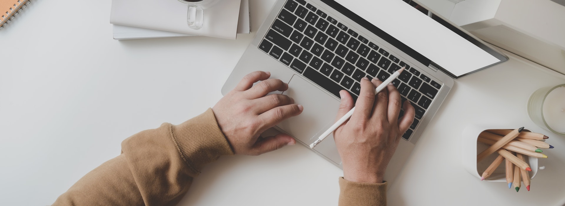 Deux mains sur un clavier à côté d’une tasse de café