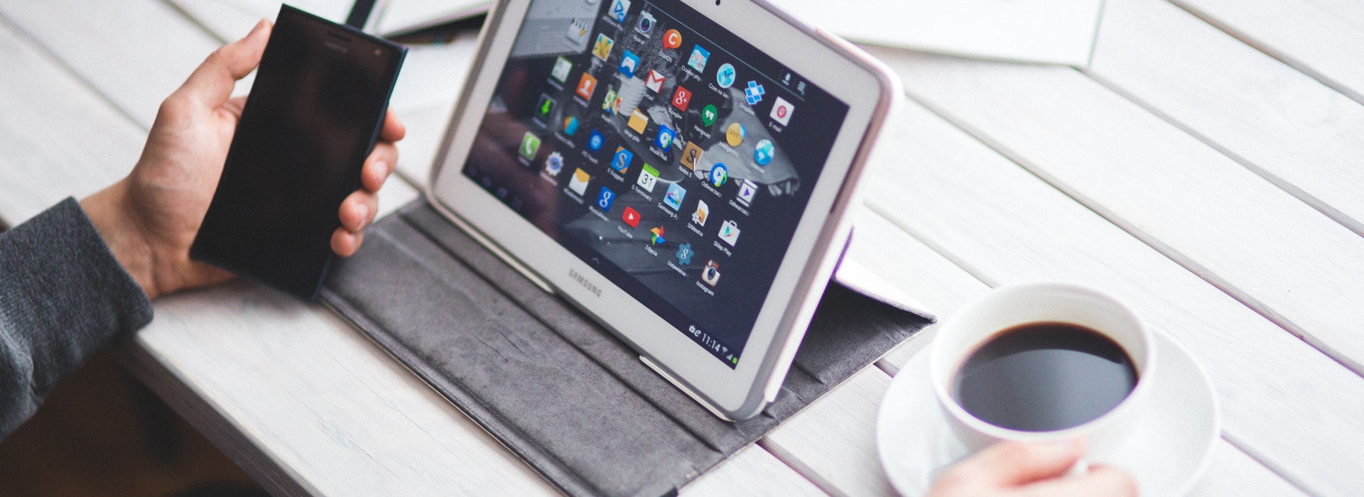 Photo of a tablet, cup of coffee and smartphone on white desk