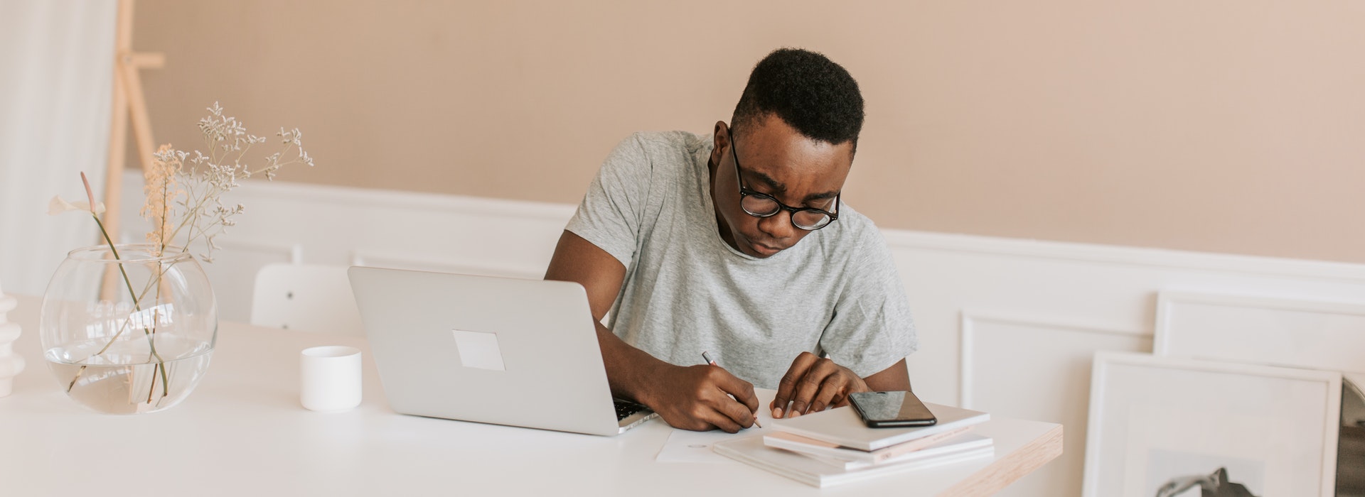 Photo of young man writing in notebook beside laptop